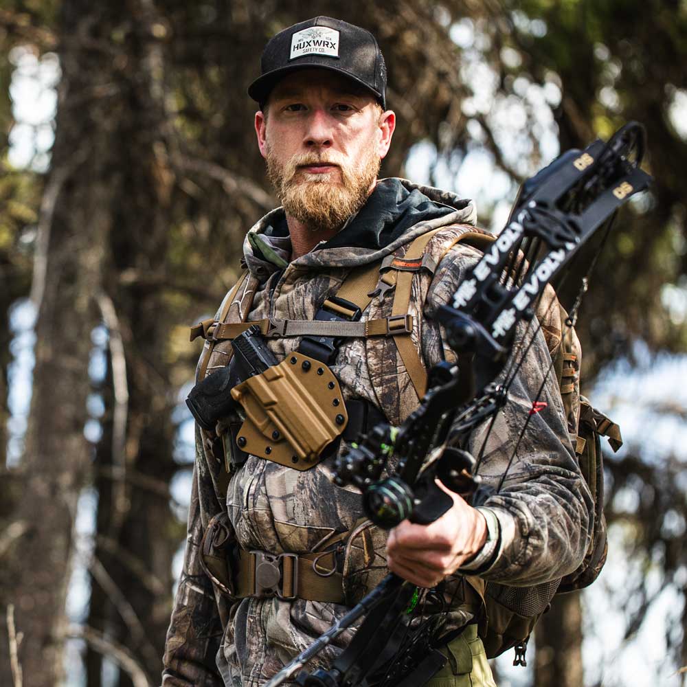 person in hunting camouflage, with a bow. Wearing a Recon chest holster