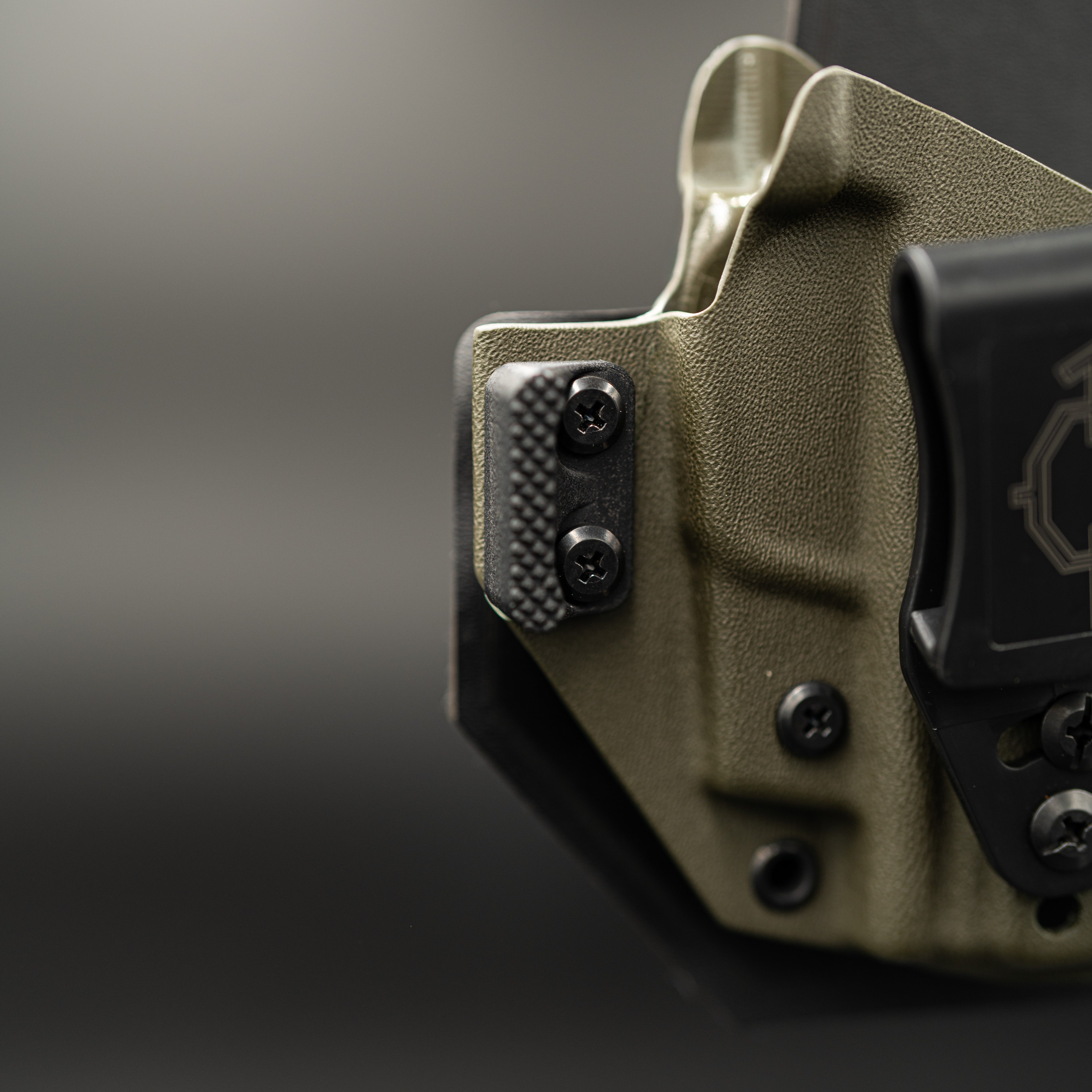 Close-up of a green outlaw IWB(inside the waistband) holster with retention screws on a blurred background
