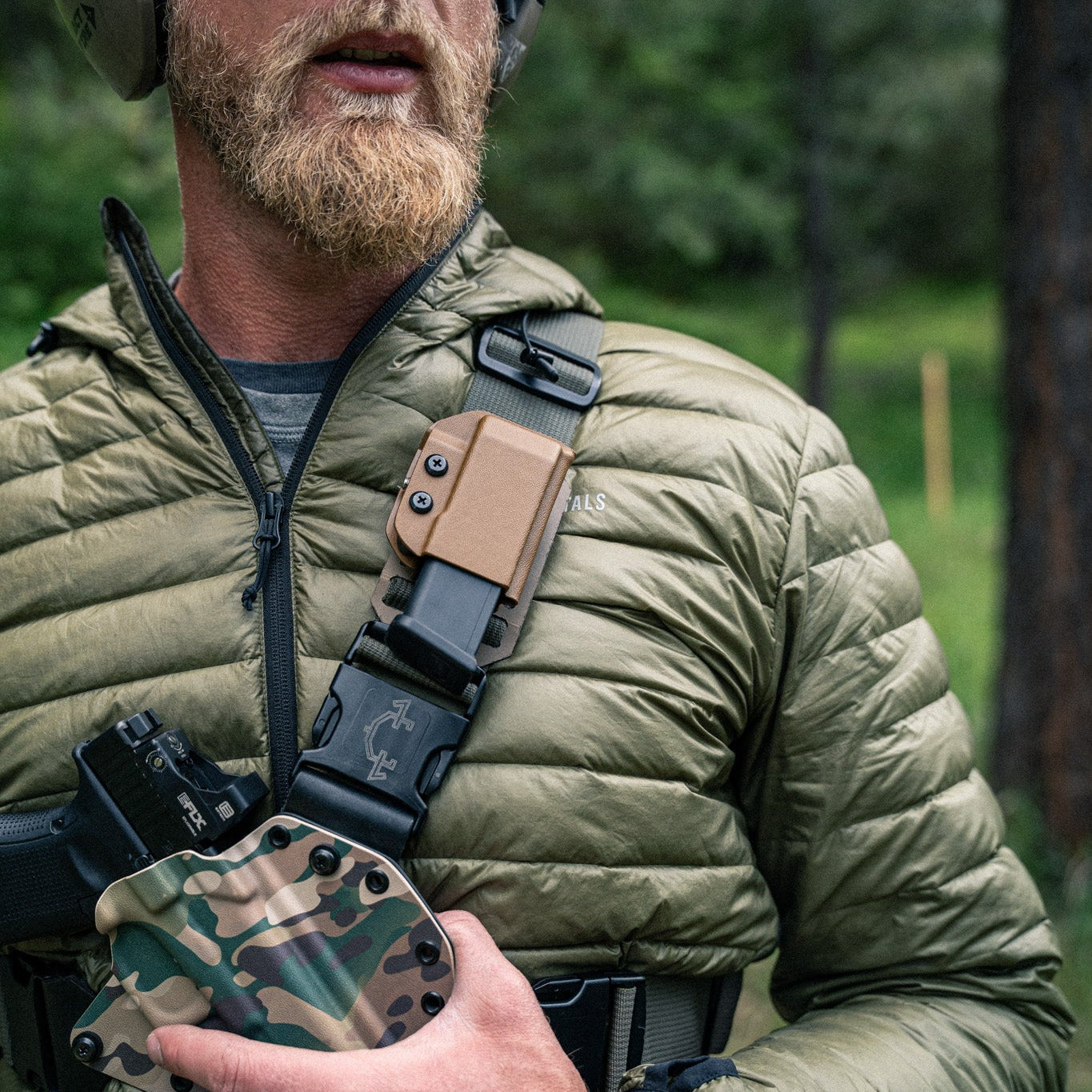 Man in outdoor setting wearing tactical gear and holding a camouflage pouch.