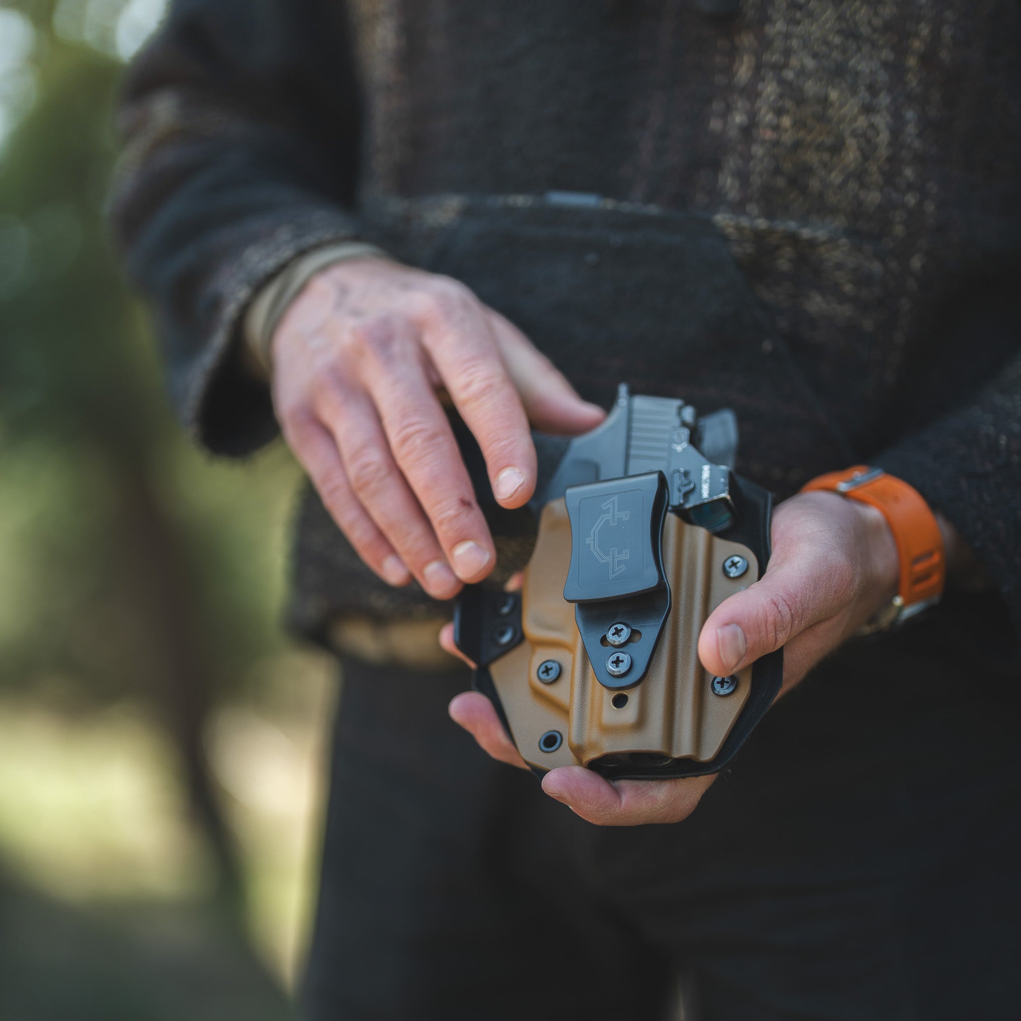 Person holding an IWB(inside the waistband) holster with a blurred natural background