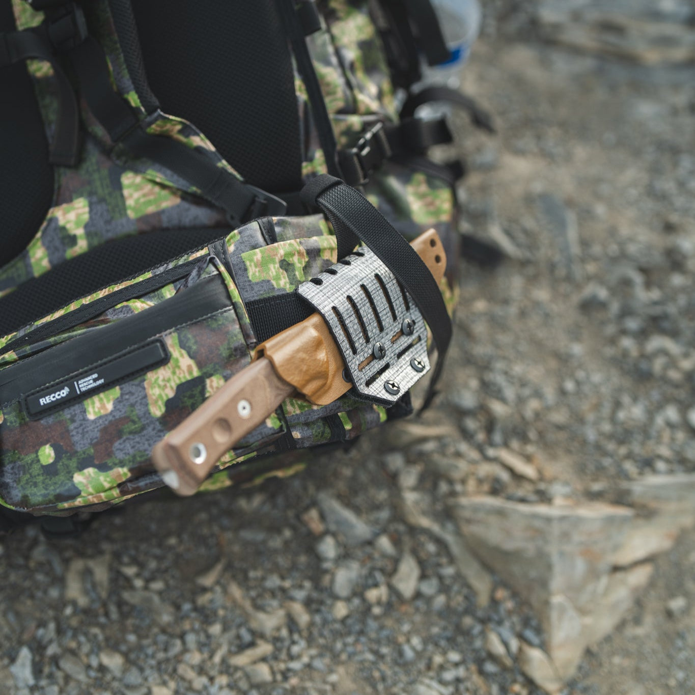 Camouflage backpack with a knife attached with a blade lok on a rocky ground