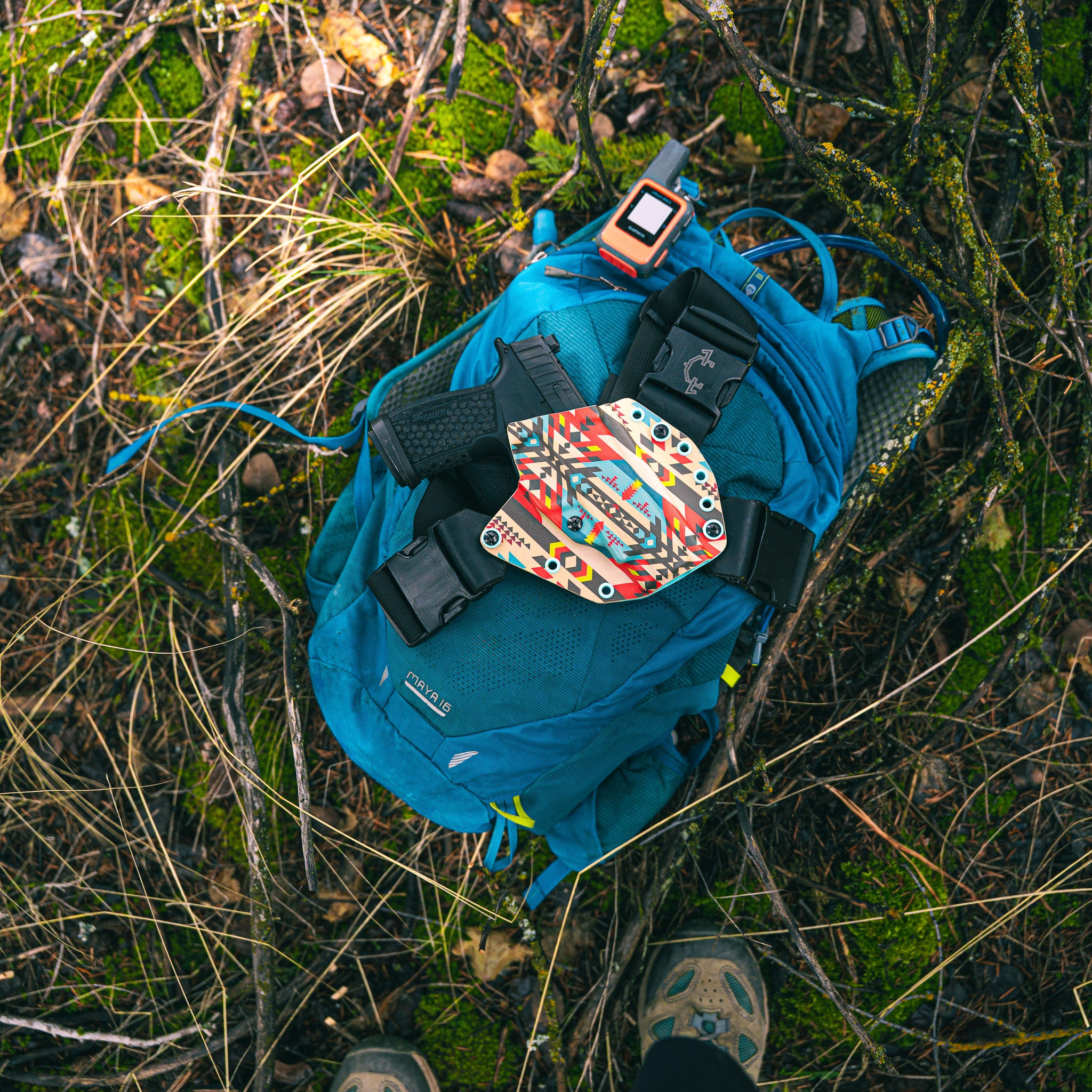 Blue backpack with colorful patch on a grassy ground with a ladies recon chest holster