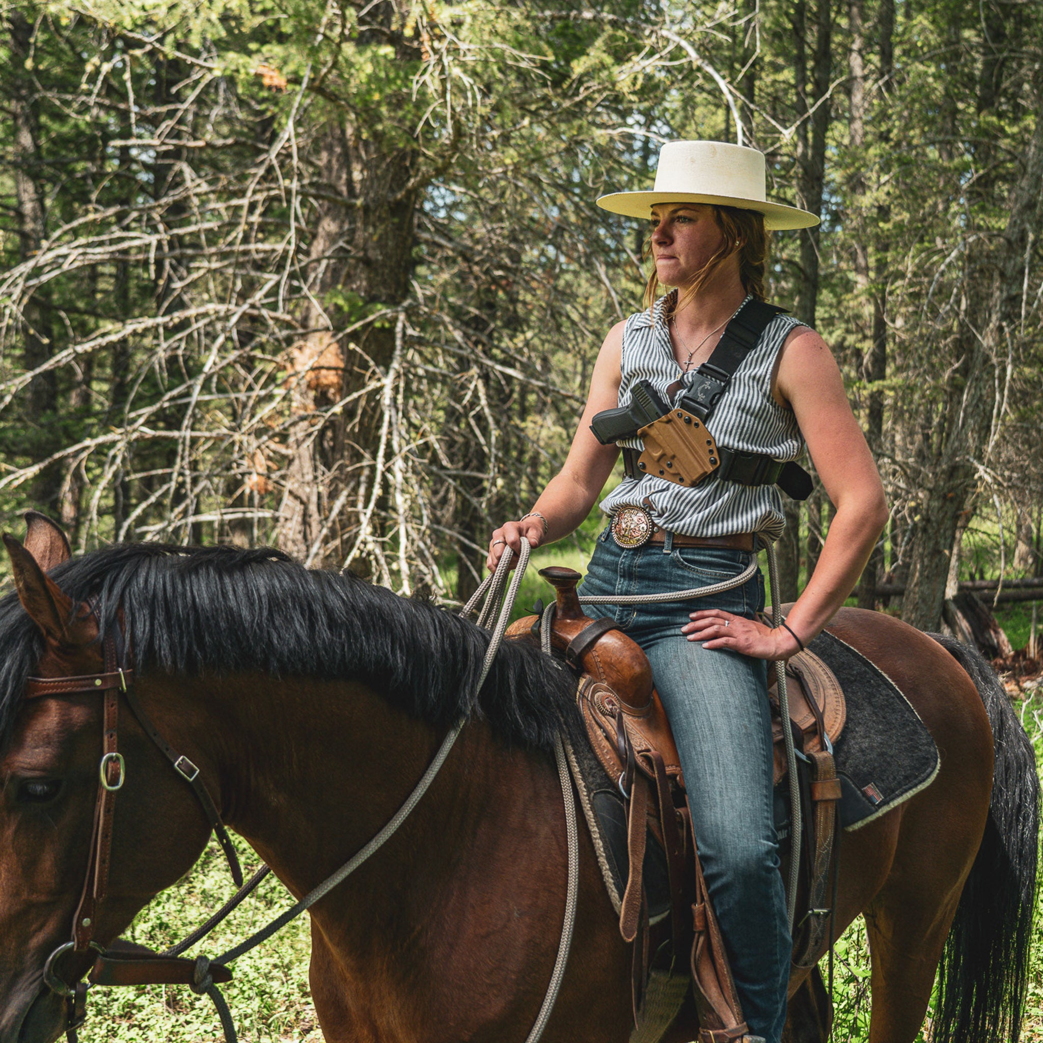 Woman in cowboy hat sitting on a horse in a forest setting and wearing a ladies recon chest holster