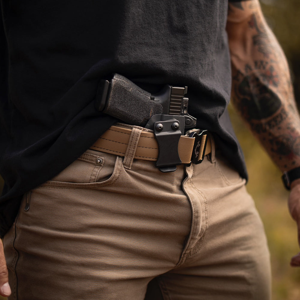 Person wearing a tactical edc(everyday carry) belt with a iwb(inside the waistband) holster standing outdoors.