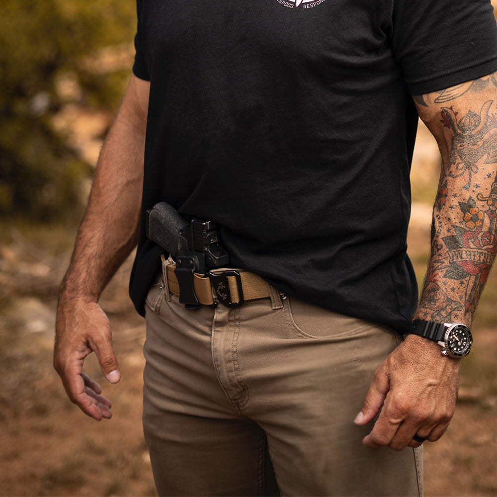 Person wearing a black t-shirt, beige pants, and an edc(everyday carry) belt with a blurred natural background