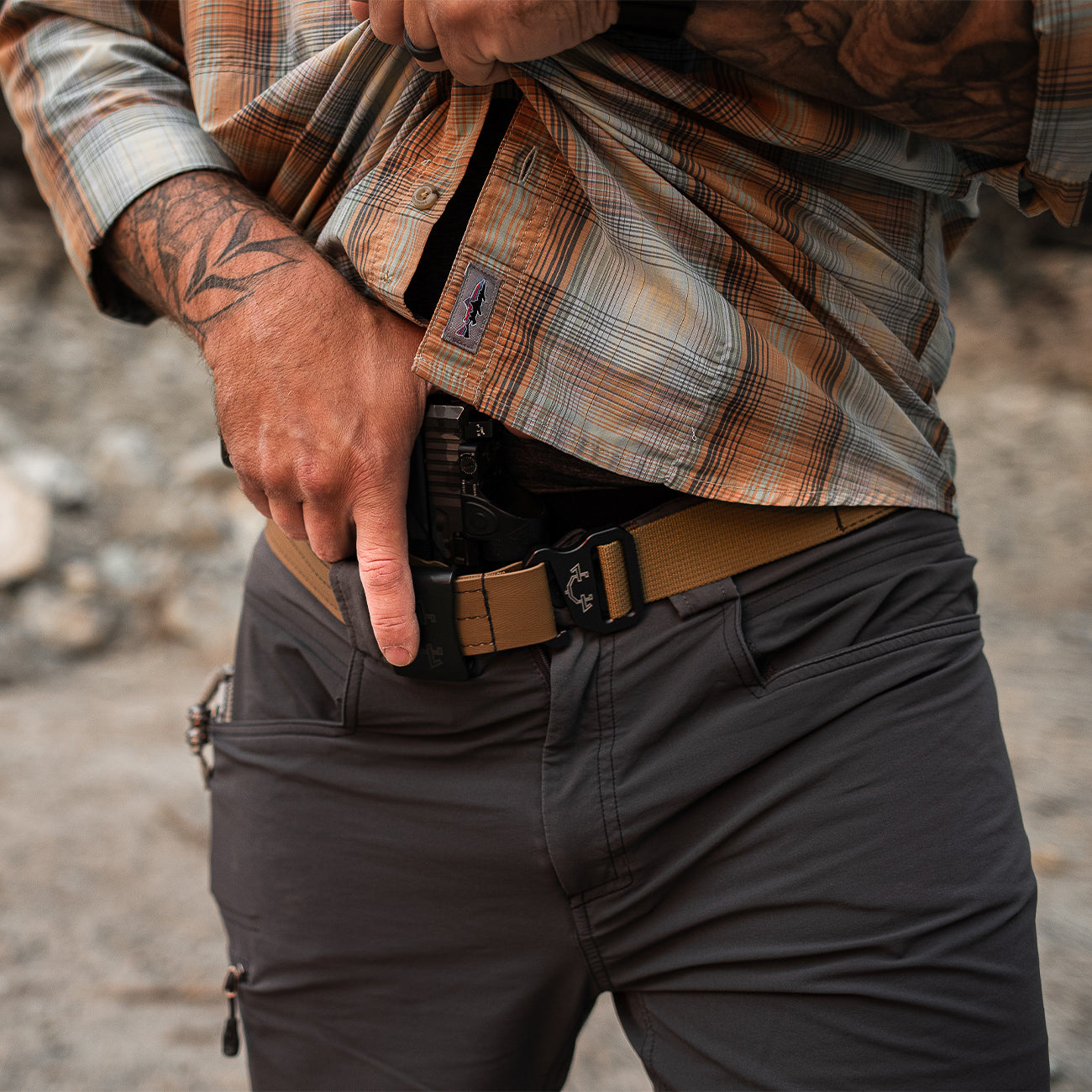 Person wearing a plaid shirt and dark pants with a edc(everyday carry) belt and standard iwb(inside the waistband) holster outdoors.