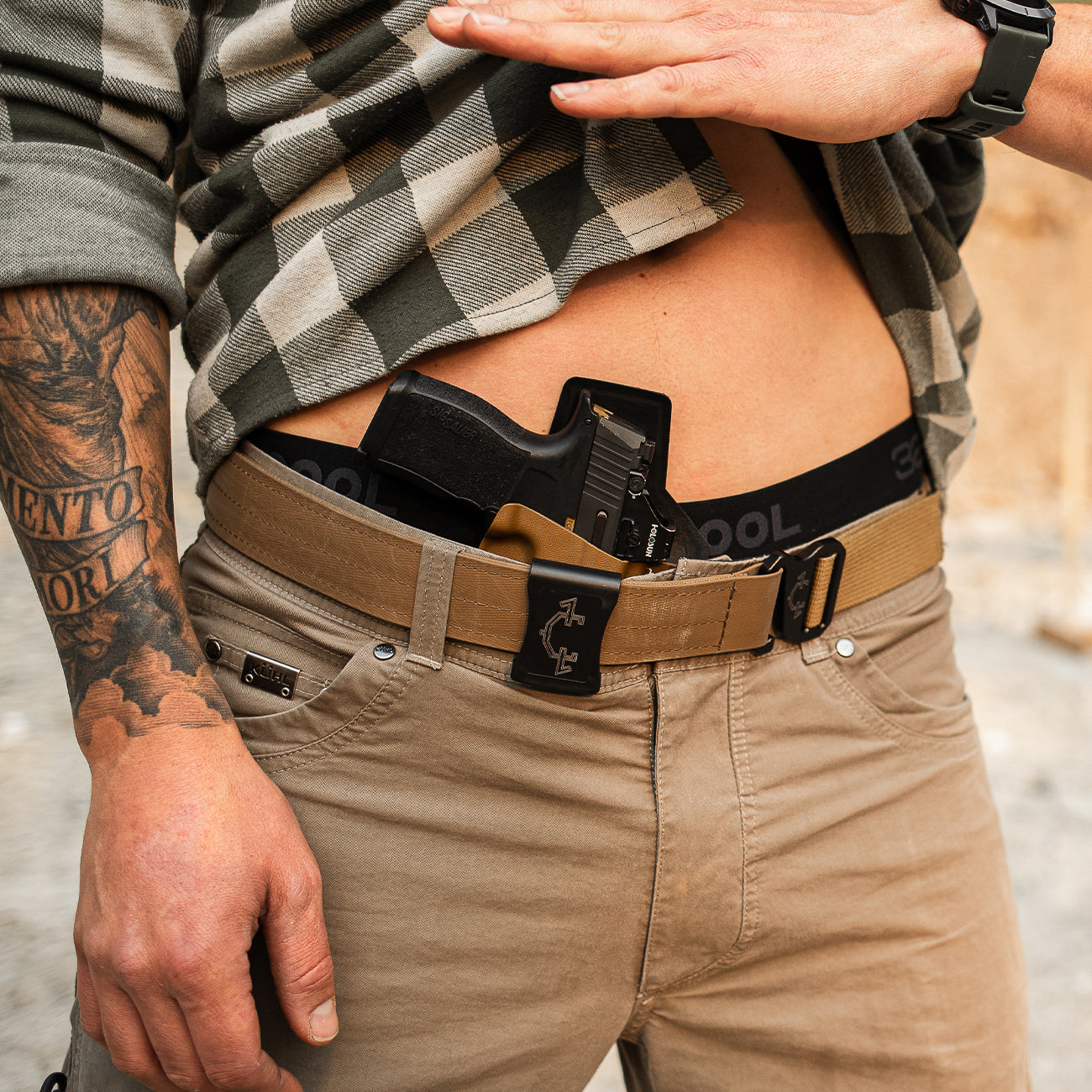 Person wearing an edc(everyday carry) belt and outlaw iwb(inside the waistband) with a plaid shirt and tattooed arm.