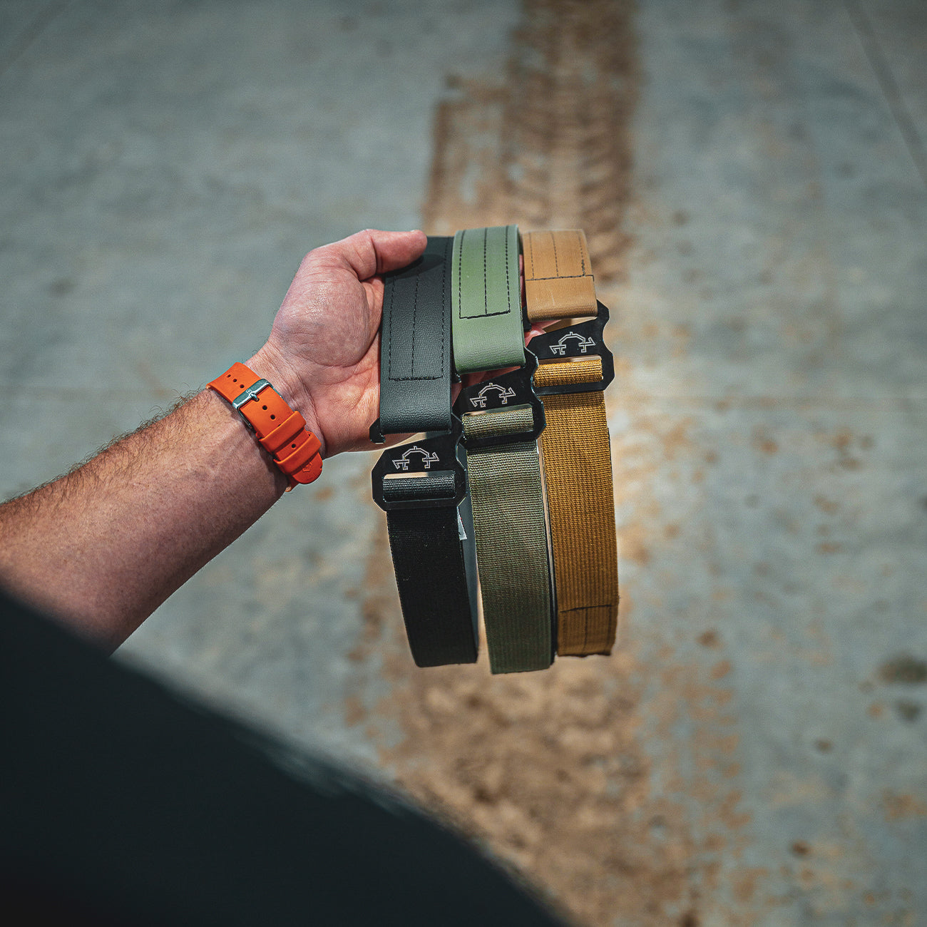 Hand holding edc(everyday carry) belts of different colors against a textured background