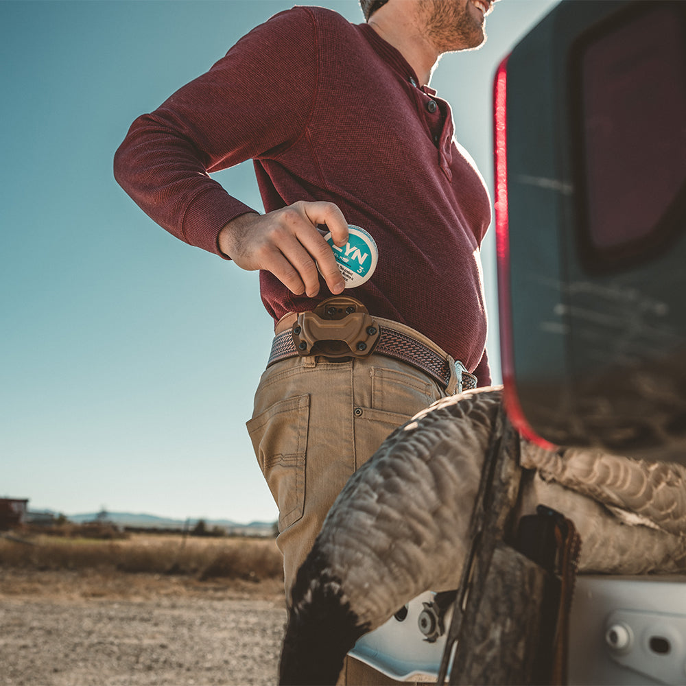 Man holding a can of zyn for his pouch holster attached to his edc(everyday carry) belt next to a truck in an open field