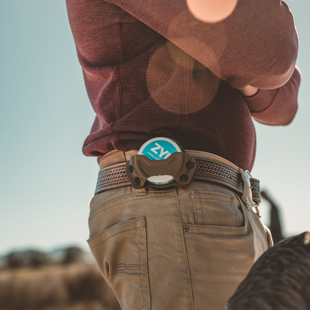 Person wearing a red shirt and beige pants with a pouch holster attached to an edc(everyday carry) belt standing outdoors.