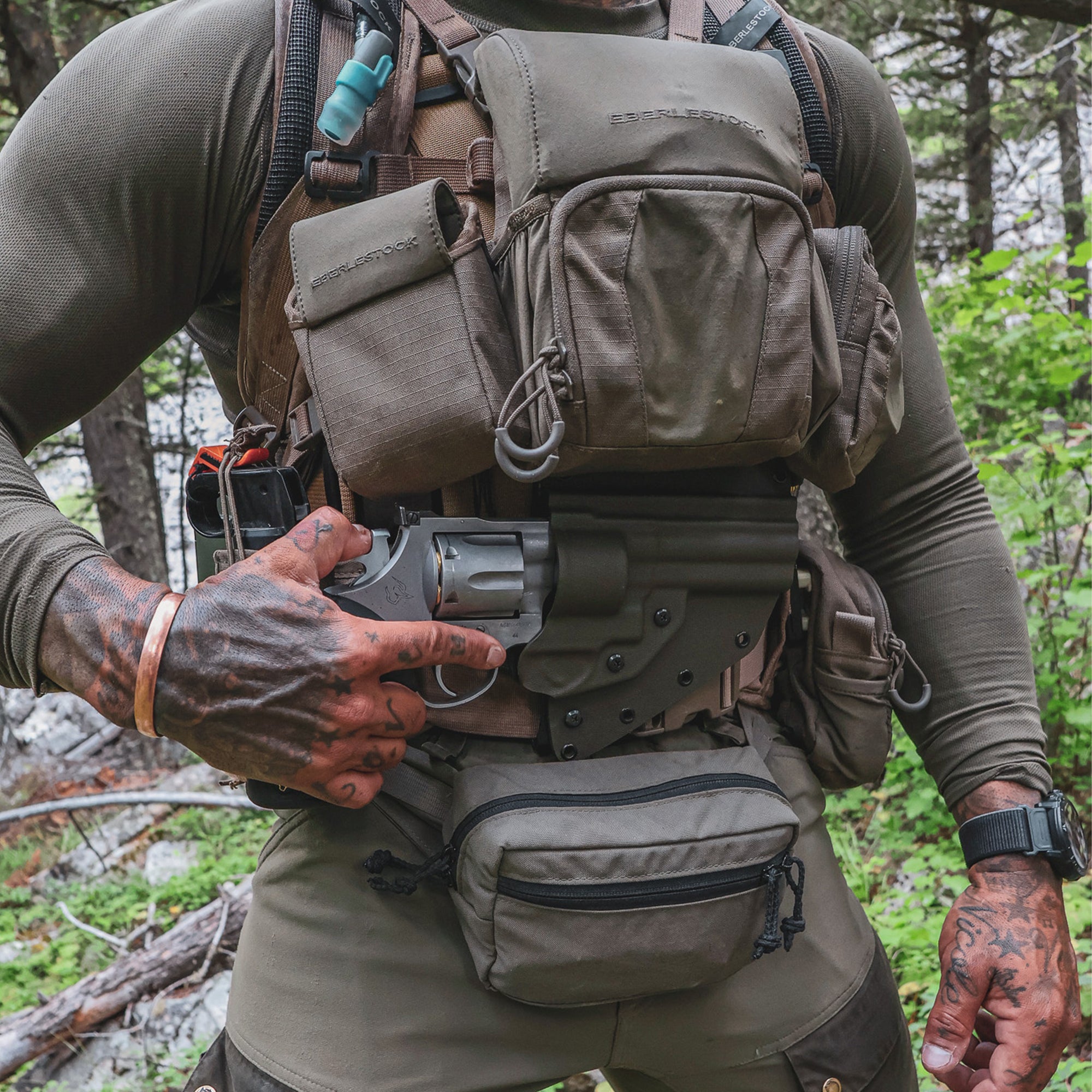 person wearing a Eberlestock backpack along with a eberlestock bino harness, on top of a Guide torso holster, in the wilderness.