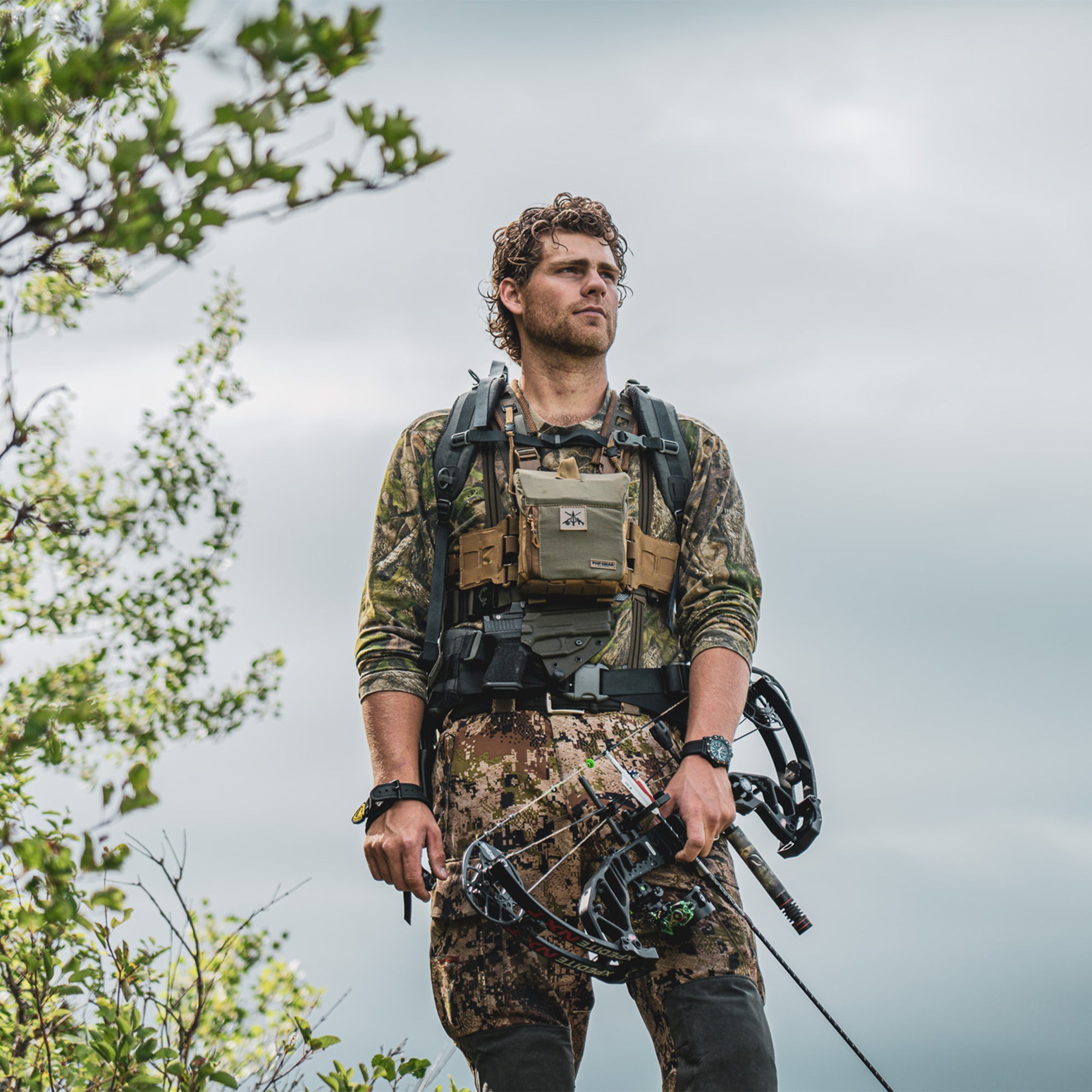 Person on a high mountain, in bow archery gear, and a guide torso holster.