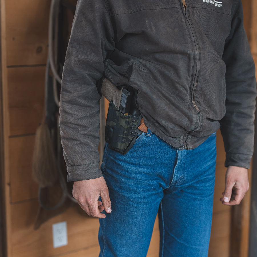 Person wearing a black jacket and blue jeans with an outlaw owb(outside the waistband)