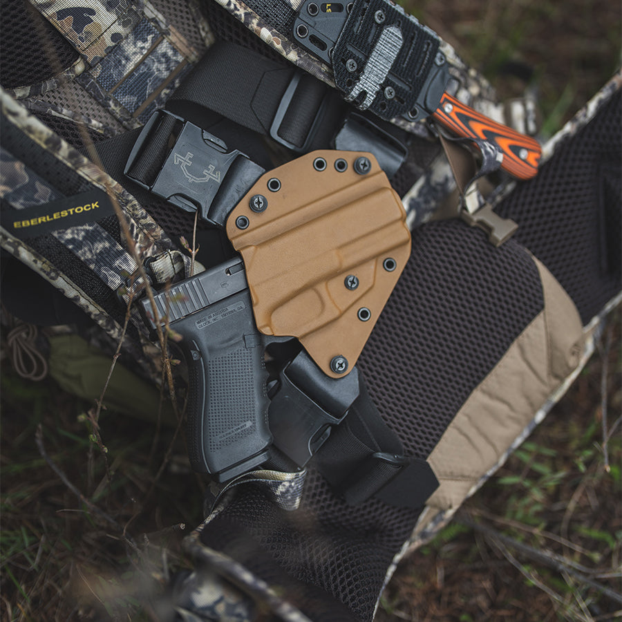 Black and tan recon chest holster on a camouflage surface.