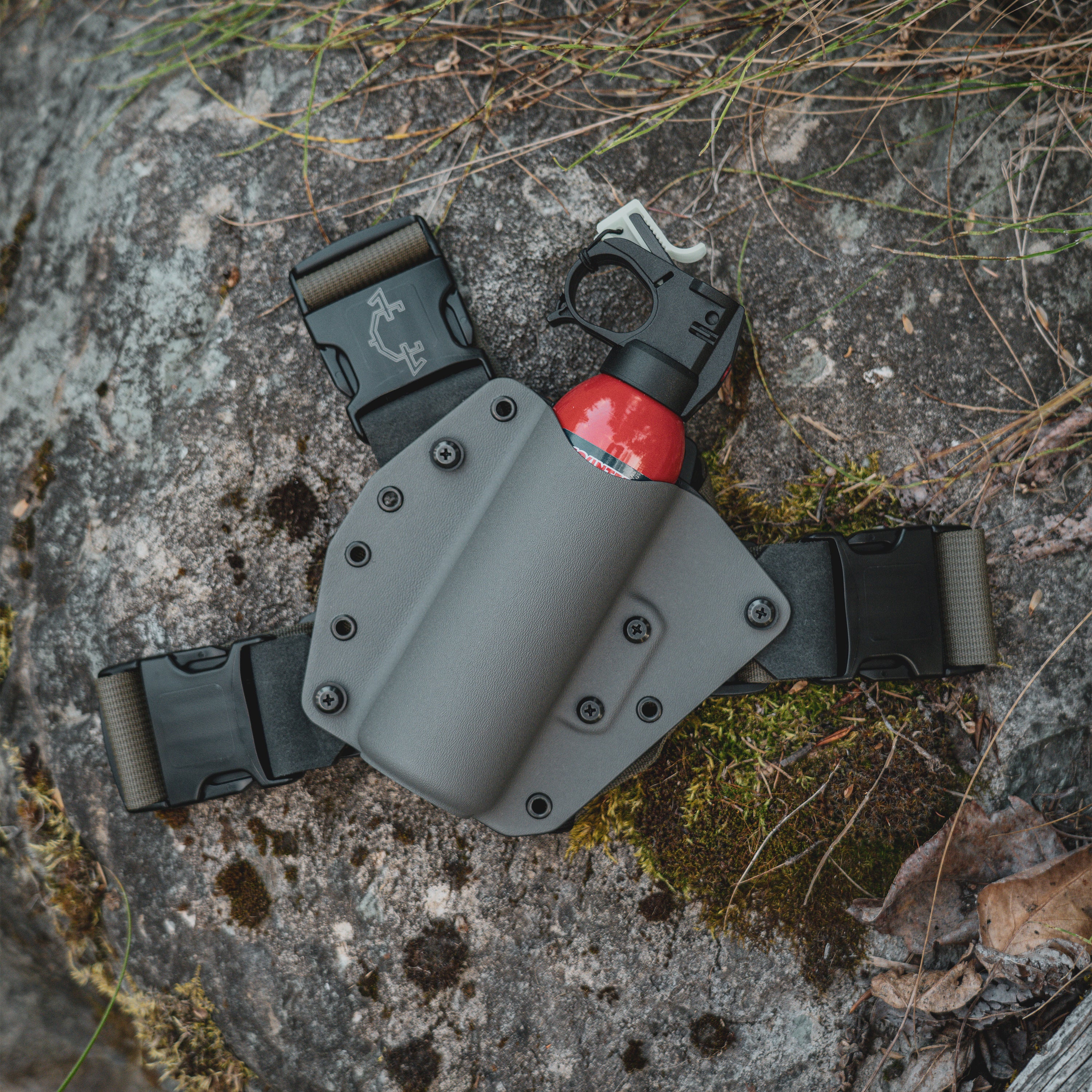 Gray bear spray chest holster with red bear spray on a textured stone surface