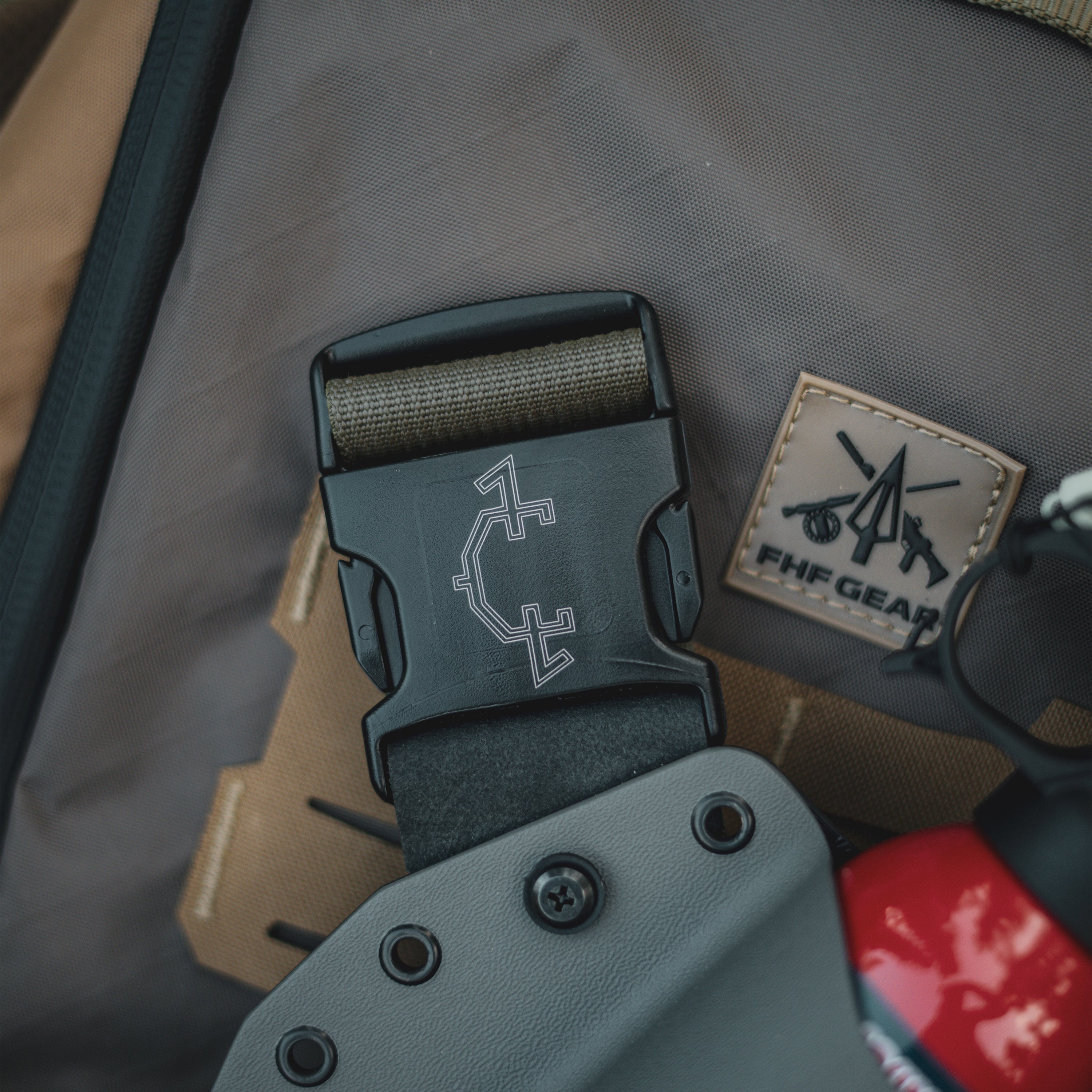 Close-up of a bear spray chest holster with a branded buckle on a gray bag.