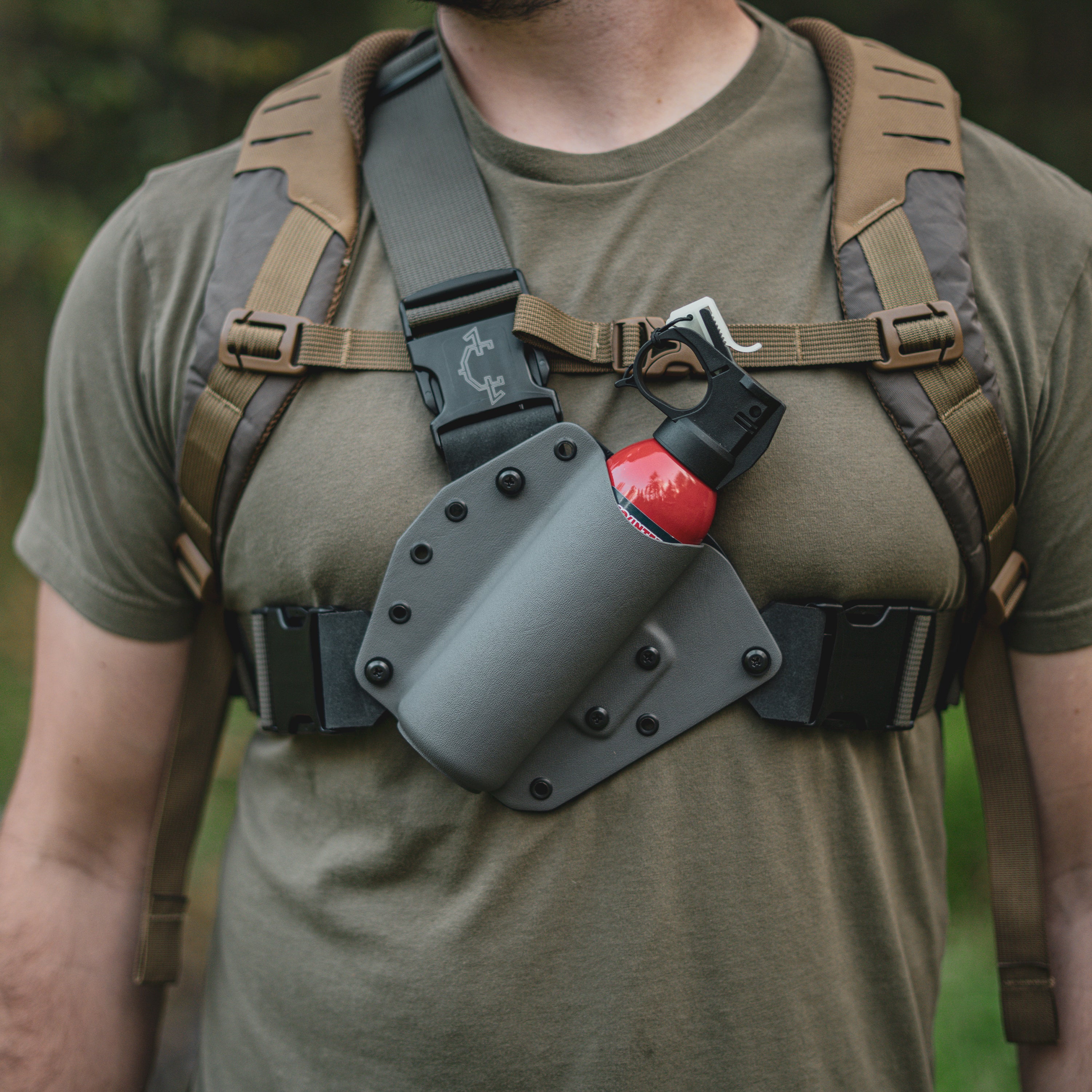 Person wearing a bear spray chest holster with a red bear spray attached outdoors.