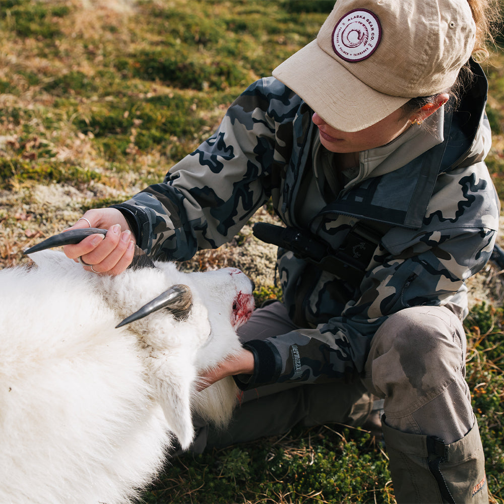 Woman in camouflage jacket and beige cap handling a mountain goat outdoors and wearing a ladies recon chest holster