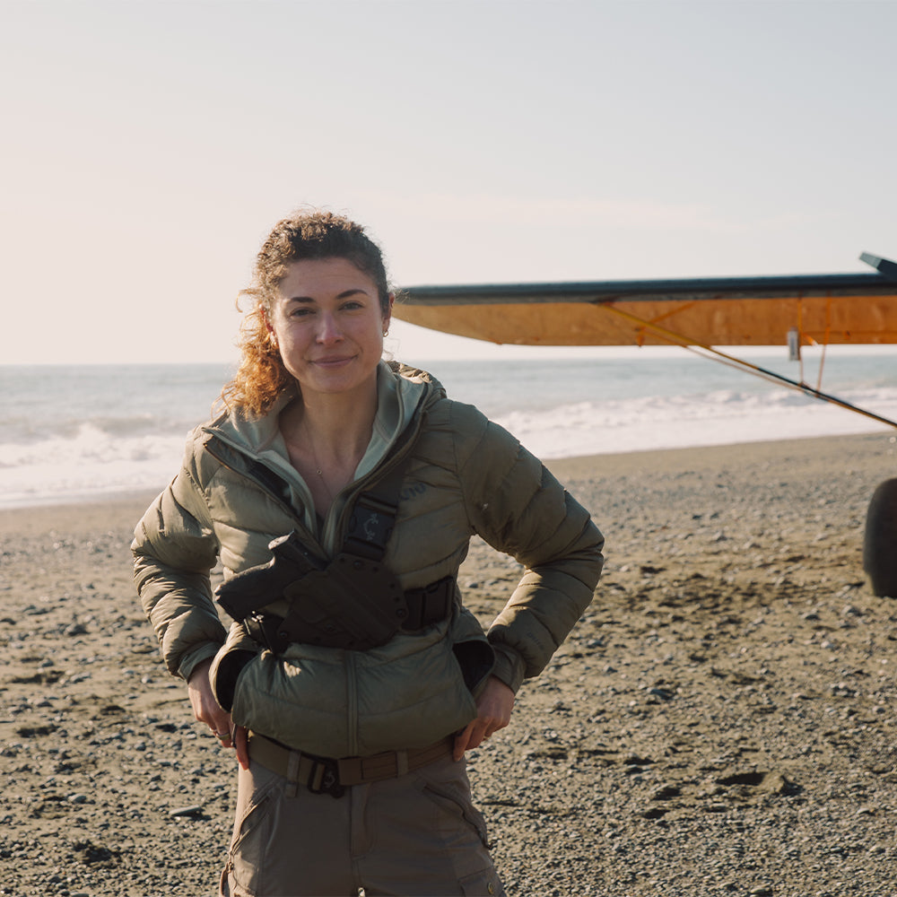 Woman standing on a beach with a small airplane in the background and wearing a ladies recon chest holster
