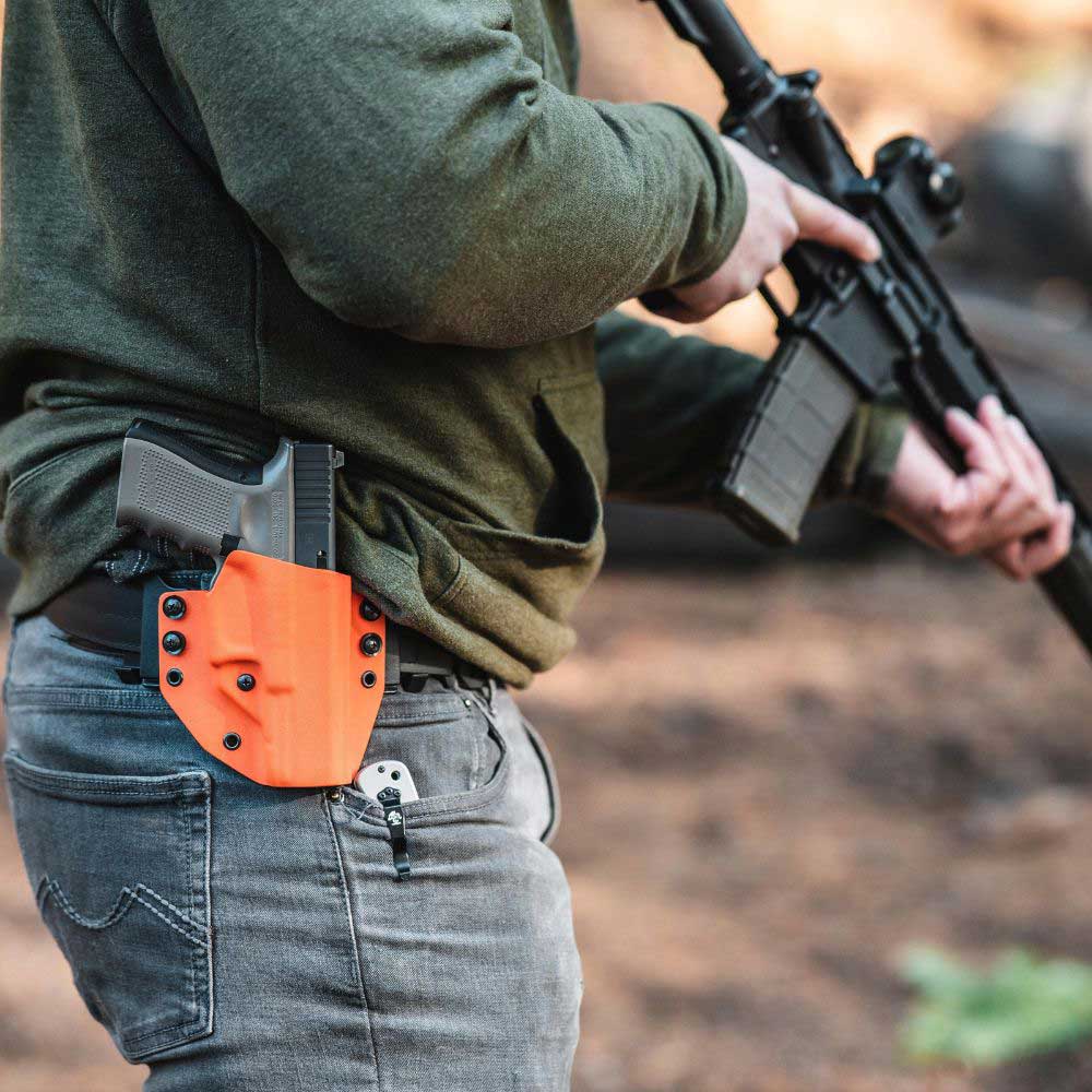 Person wearing a standard owb(outside the waistband) holster while holding a rifle