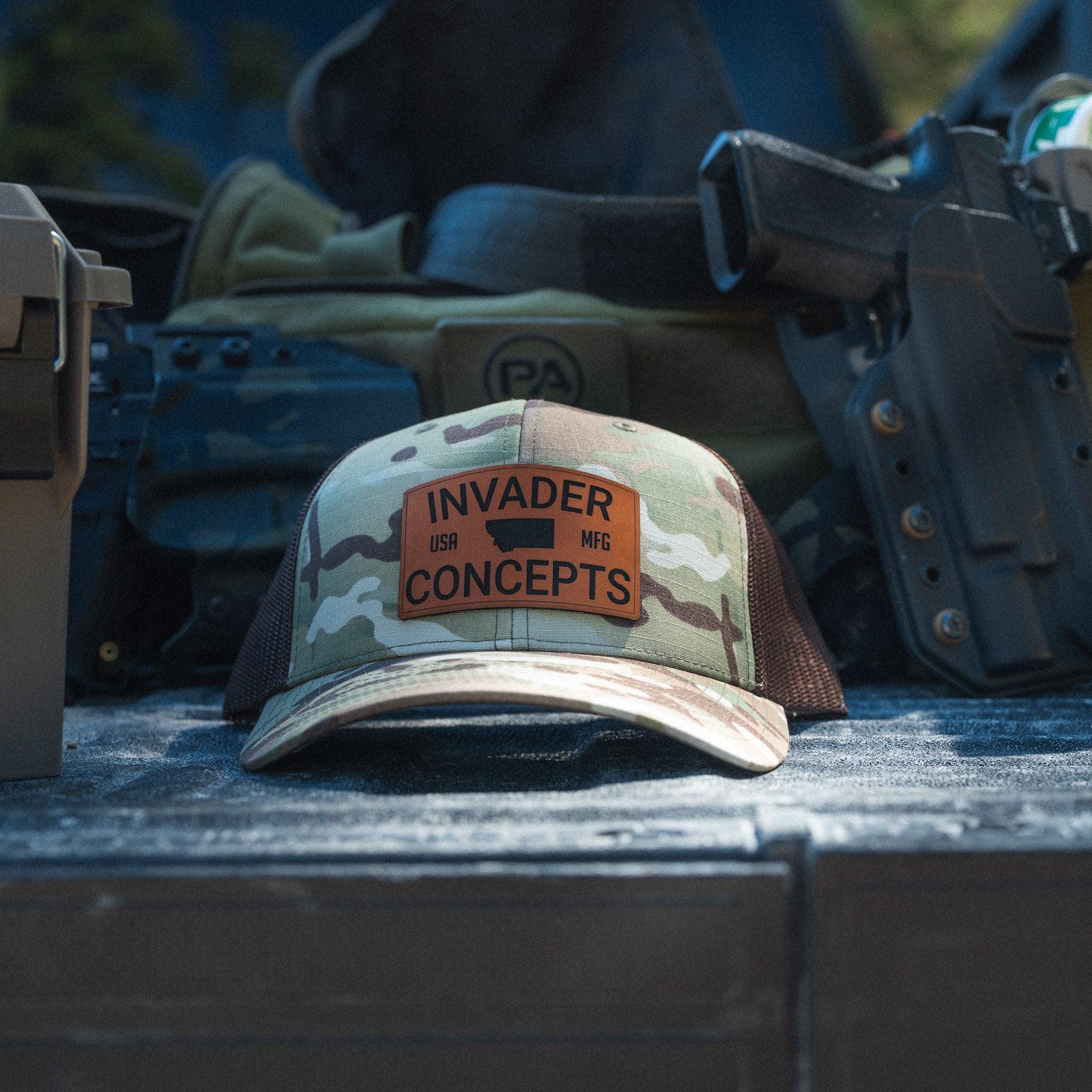 Camouflage cap with 'Invader USA Concepts' patch on a military-style background