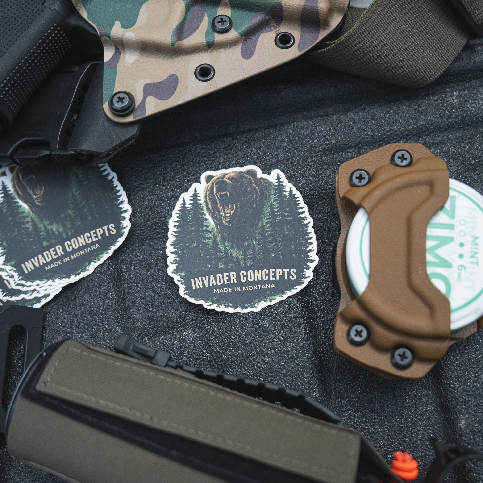 Invader Concepts products including a knife, holster, and stickers on a textured surface.