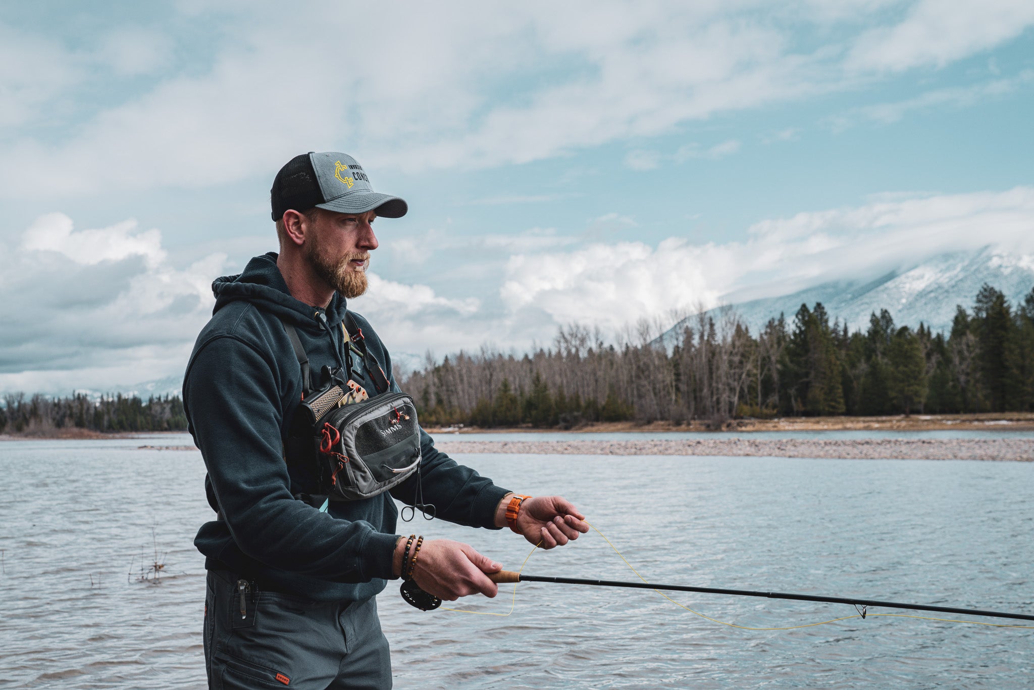 Man fly fishing with a Recon chest holster from Invader Concepts in the backcountry