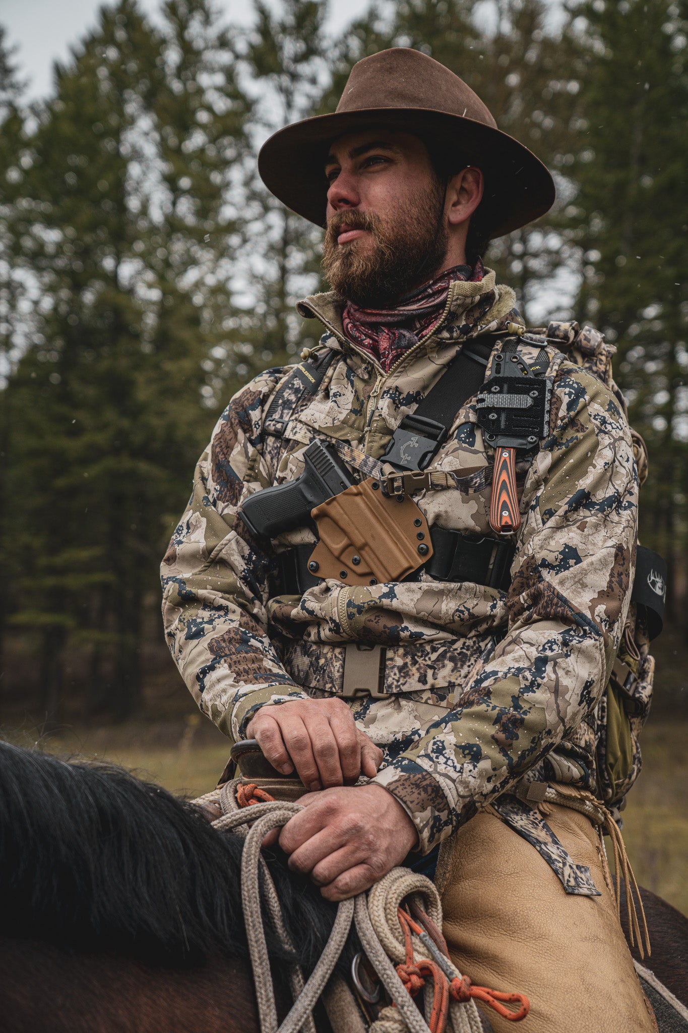 Man wearing a Recon chest holster from Invader Concepts while riding a horse in the backcountry