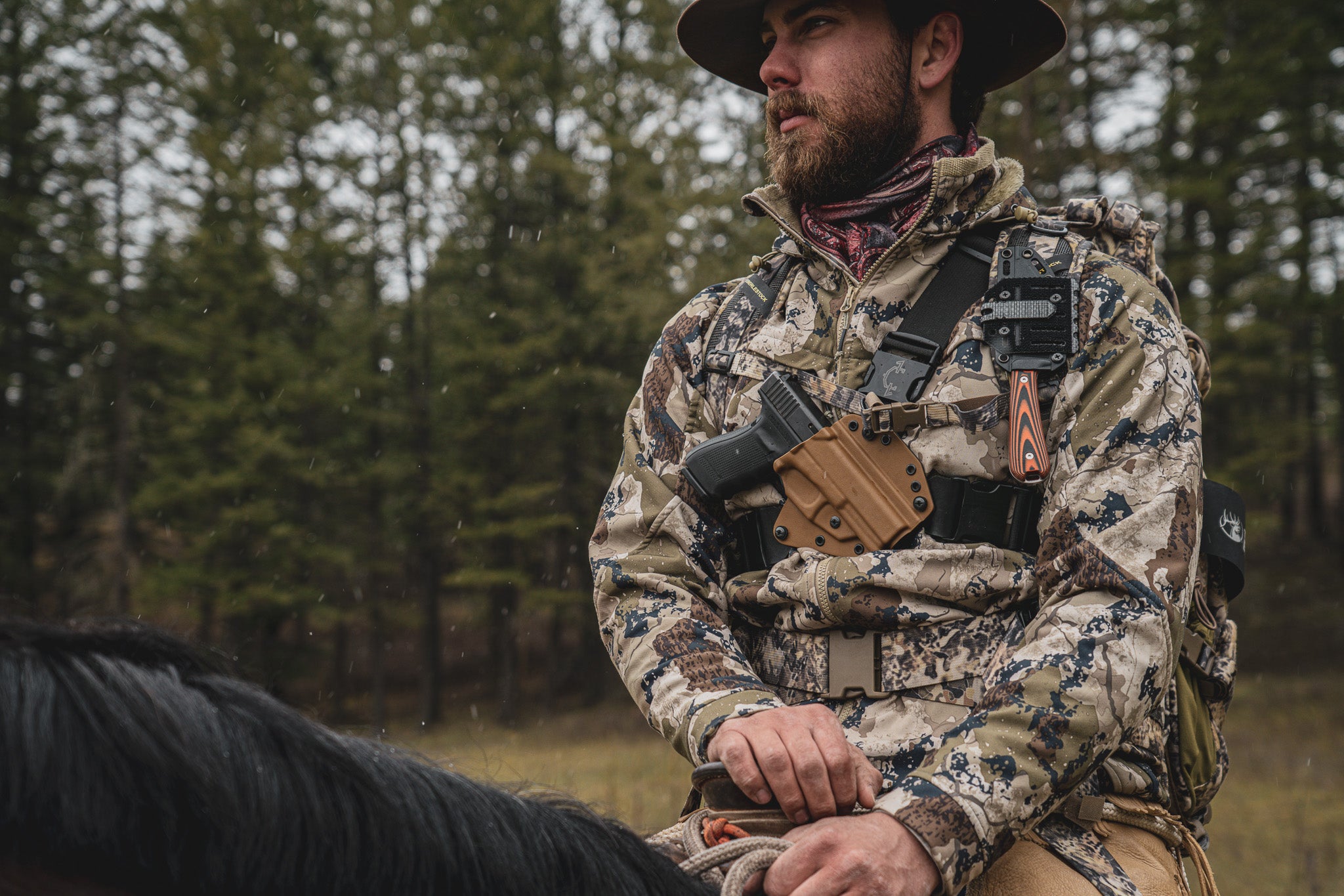 Man riding a horse while wearing a Recon chest holster from Invader Concepts in the backcountry