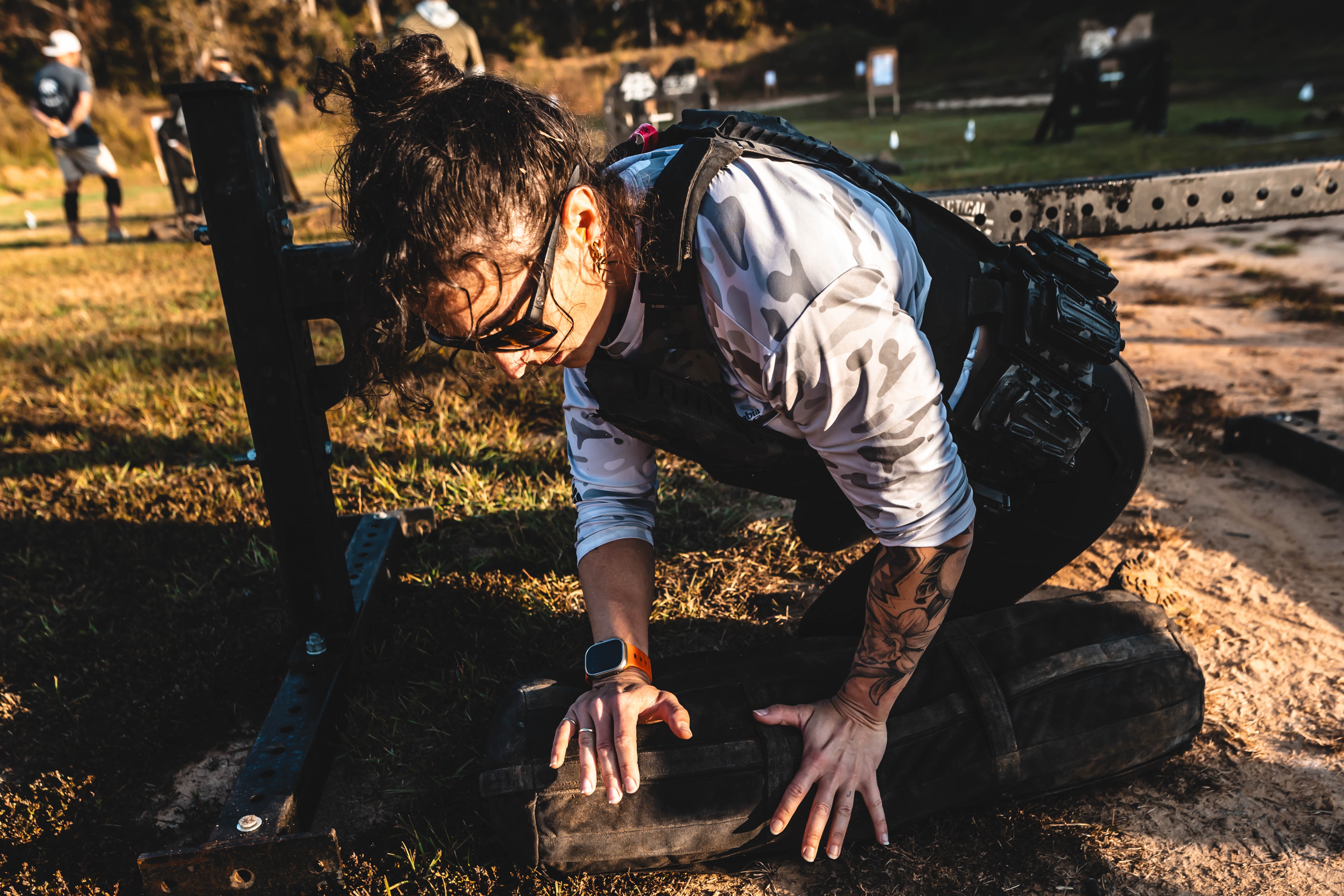 Person in tactical gear kneeling on a log outdoors